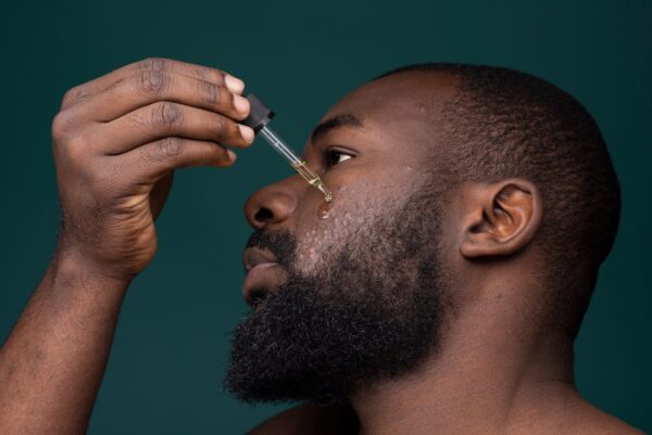 african,bearded,man,with,pimples,and,skin,problems,applying,oil